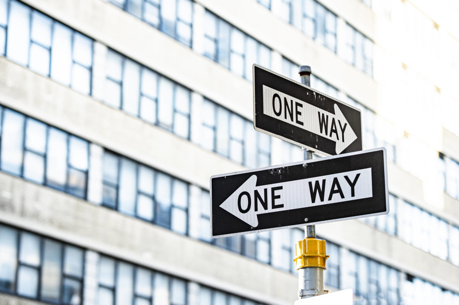 Close-up view of 'one way' road sign with blurred building in the background. Manhattan, New York City, United States of America.